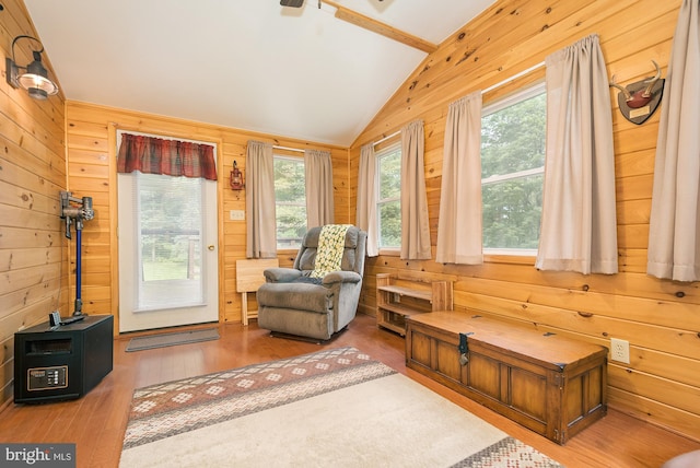 living area with lofted ceiling, wood walls, hardwood / wood-style flooring, and a healthy amount of sunlight