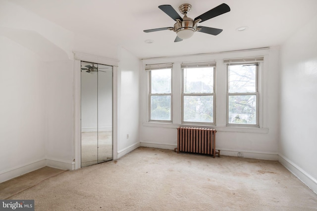 unfurnished bedroom featuring radiator heating unit, a closet, ceiling fan, and light colored carpet