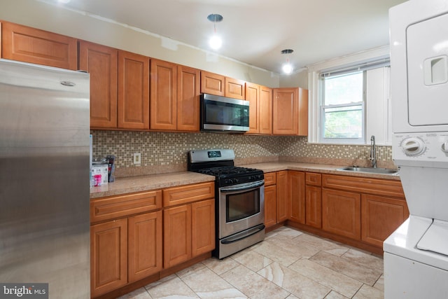 kitchen featuring hanging light fixtures, decorative backsplash, stainless steel appliances, stacked washer and dryer, and sink