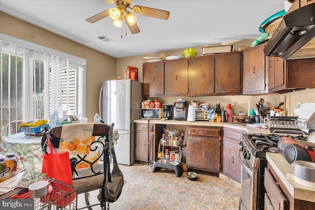 kitchen with stainless steel gas range oven, white fridge, ceiling fan, and extractor fan