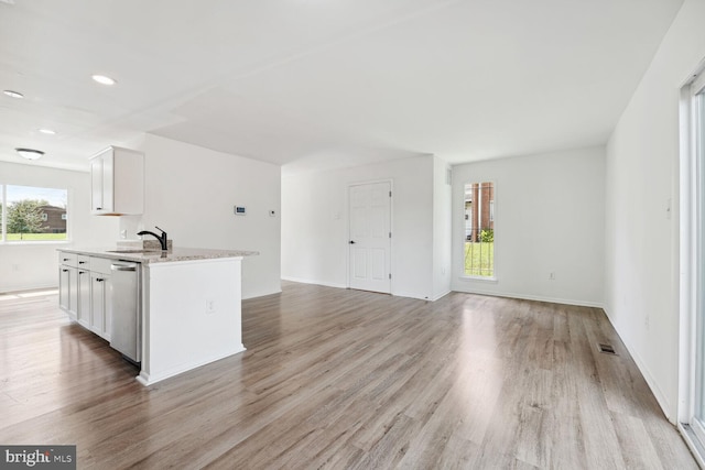 kitchen featuring light wood-type flooring, white cabinets, stainless steel dishwasher, and light stone countertops