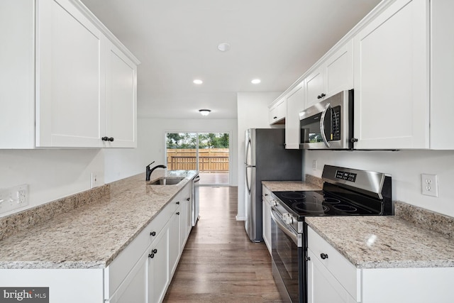 kitchen with appliances with stainless steel finishes, white cabinets, light stone countertops, wood-type flooring, and sink