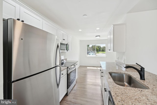 kitchen with appliances with stainless steel finishes, sink, white cabinetry, light hardwood / wood-style floors, and light stone counters