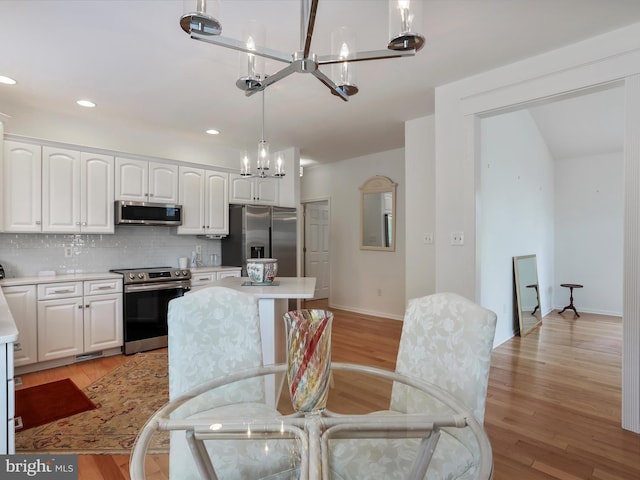 kitchen featuring light wood-type flooring, stainless steel appliances, hanging light fixtures, backsplash, and white cabinets