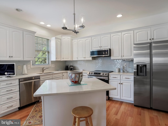 kitchen featuring hanging light fixtures, white cabinetry, stainless steel appliances, and sink