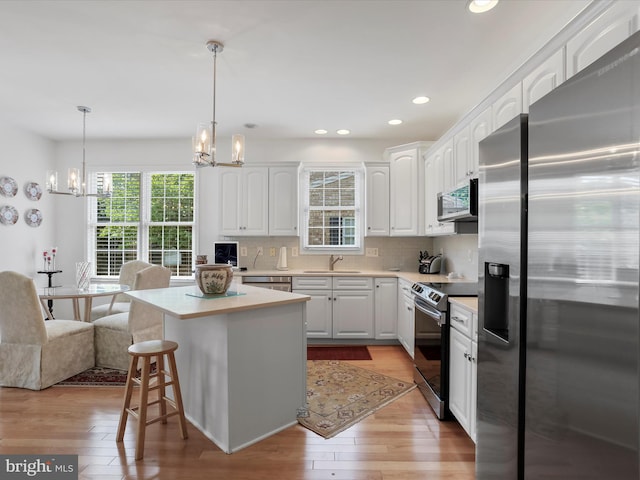 kitchen featuring white cabinetry, hanging light fixtures, a center island, tasteful backsplash, and appliances with stainless steel finishes