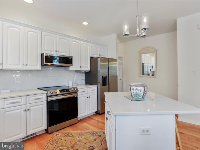 kitchen featuring a kitchen island, white cabinets, stainless steel appliances, and hanging light fixtures