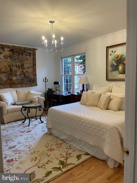 bedroom with hardwood / wood-style flooring, ornamental molding, and a notable chandelier