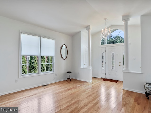 entryway with light hardwood / wood-style floors, high vaulted ceiling, ornate columns, and a notable chandelier