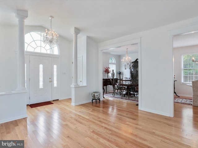 entryway featuring light hardwood / wood-style flooring, vaulted ceiling, an inviting chandelier, and decorative columns