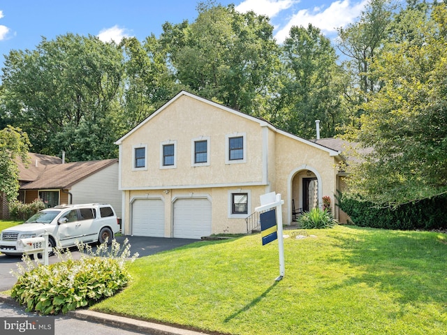 tri-level home with an attached garage, driveway, a front yard, and stucco siding