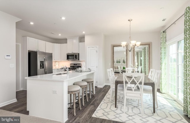 kitchen featuring a kitchen island with sink, an inviting chandelier, dark wood-type flooring, white cabinets, and appliances with stainless steel finishes