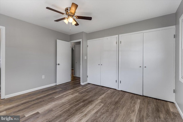 unfurnished bedroom with multiple closets, ceiling fan, and dark wood-type flooring