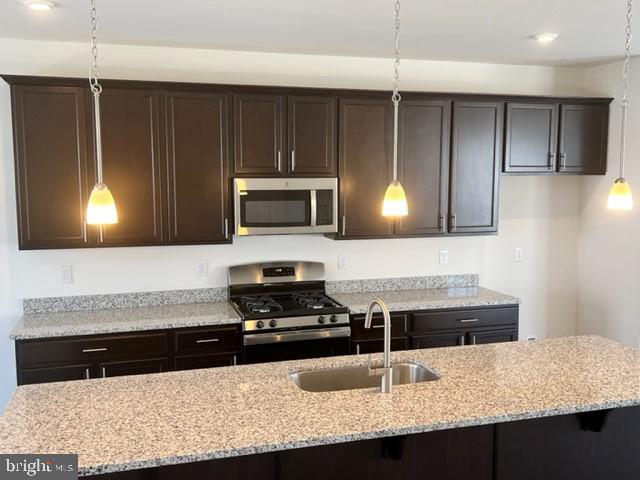 kitchen featuring appliances with stainless steel finishes, pendant lighting, dark brown cabinetry, light stone countertops, and sink