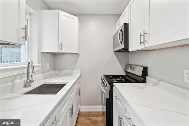 kitchen with white cabinetry, light stone countertops, light hardwood / wood-style floors, stainless steel appliances, and sink