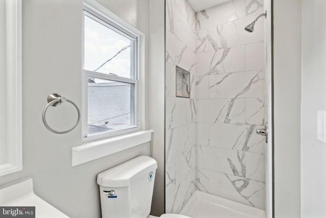 bathroom with toilet, a tile shower, and a healthy amount of sunlight