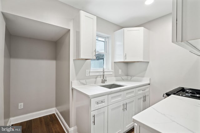 kitchen with white cabinets, dark wood-type flooring, sink, and light stone counters