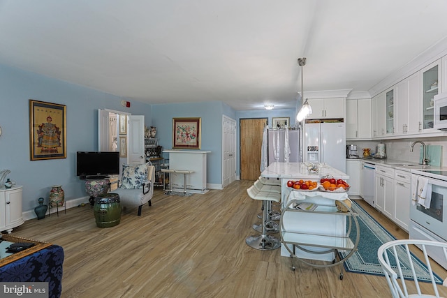 interior space with white appliances, pendant lighting, sink, white cabinetry, and light hardwood / wood-style flooring