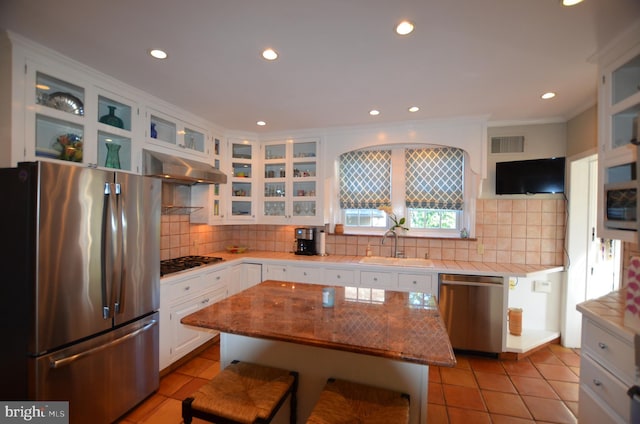 kitchen with stainless steel appliances, white cabinets, a kitchen breakfast bar, a kitchen island, and tasteful backsplash