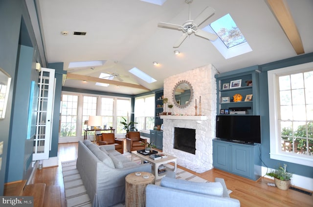 living room featuring ceiling fan, a fireplace, lofted ceiling with skylight, and light hardwood / wood-style floors