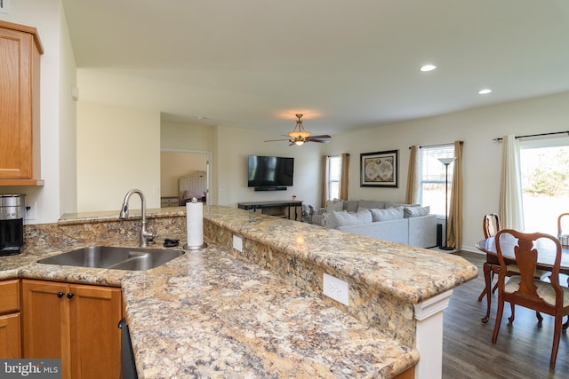 kitchen featuring dark wood-type flooring, sink, ceiling fan, light stone counters, and kitchen peninsula