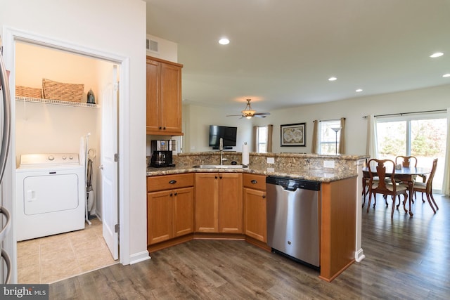 kitchen with stainless steel dishwasher, hardwood / wood-style flooring, light stone countertops, kitchen peninsula, and washer / clothes dryer