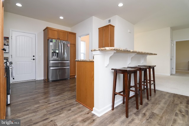 kitchen featuring a breakfast bar, light stone countertops, dark hardwood / wood-style flooring, kitchen peninsula, and stainless steel appliances