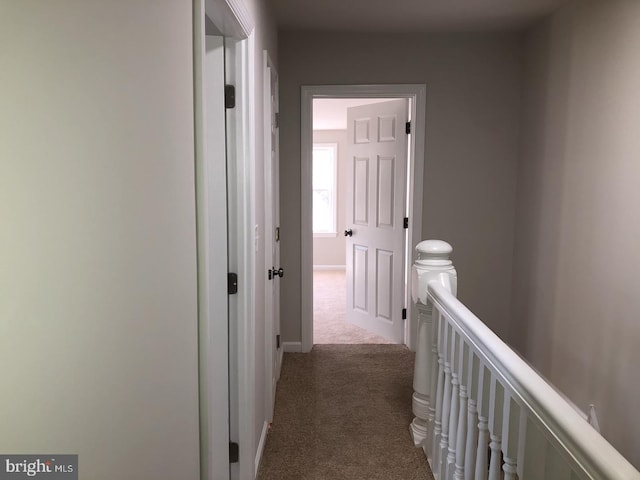 hall with dark colored carpet, an upstairs landing, and baseboards