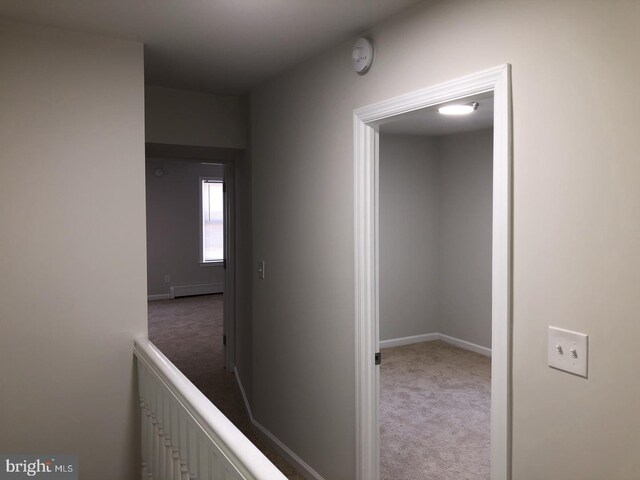 corridor featuring a baseboard heating unit and light colored carpet