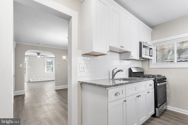 kitchen with a baseboard radiator, stainless steel appliances, sink, white cabinetry, and stone counters