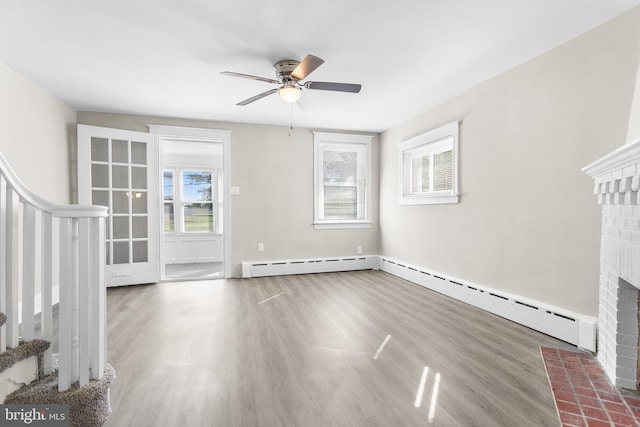 unfurnished living room featuring baseboard heating, ceiling fan, a fireplace, and wood-type flooring