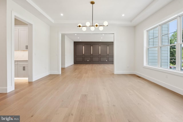 unfurnished dining area with a notable chandelier, light hardwood / wood-style flooring, and a raised ceiling