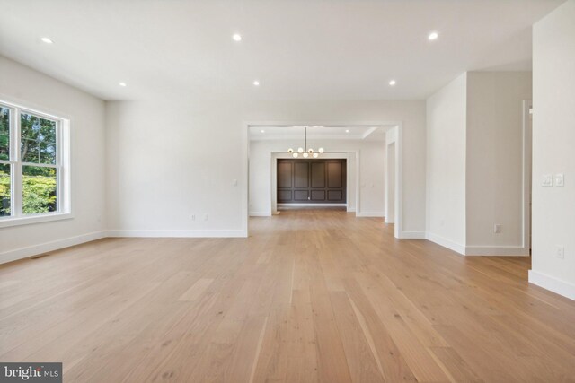 unfurnished living room with an inviting chandelier and light hardwood / wood-style floors