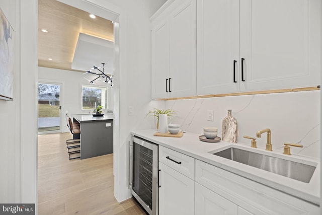 bar with white cabinetry, sink, beverage cooler, and light wood-type flooring