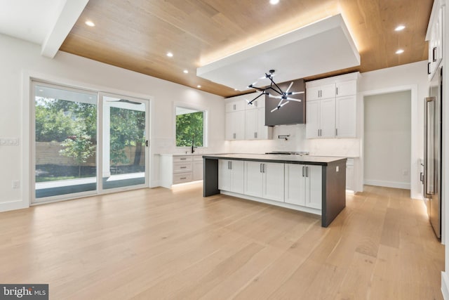 kitchen featuring decorative light fixtures, backsplash, white cabinets, a center island, and light wood-type flooring