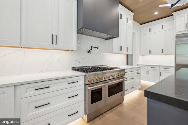 kitchen featuring high end appliances, backsplash, white cabinetry, and wall chimney exhaust hood