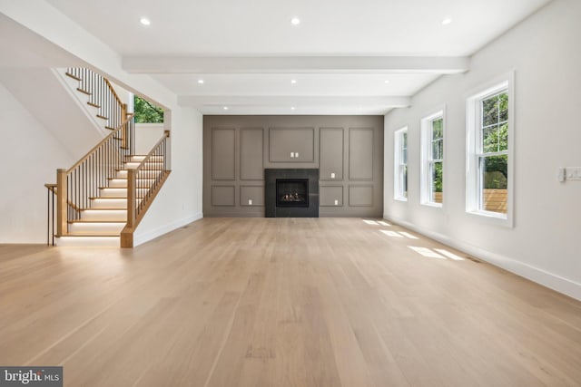 unfurnished living room with beamed ceiling and light wood-type flooring