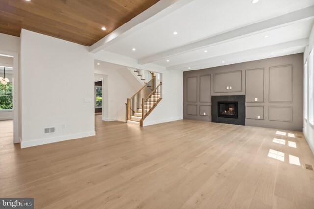 unfurnished living room with beamed ceiling, a healthy amount of sunlight, light hardwood / wood-style floors, and a tile fireplace