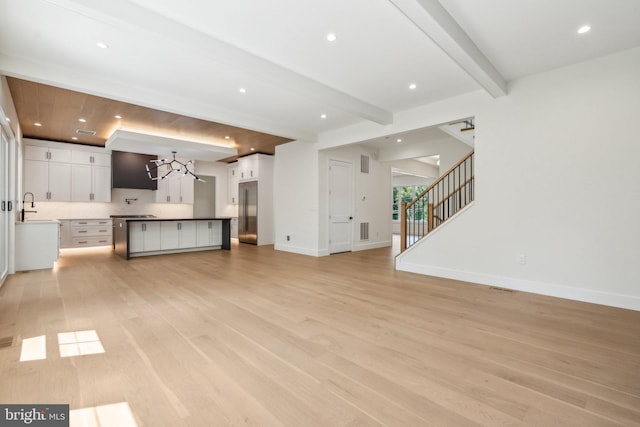 unfurnished living room featuring sink, beam ceiling, and light hardwood / wood-style flooring