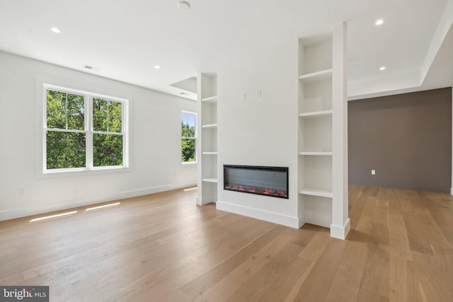 unfurnished living room featuring built in features and light wood-type flooring