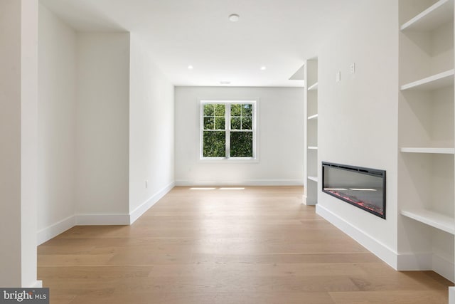 unfurnished living room with built in shelves and light hardwood / wood-style floors