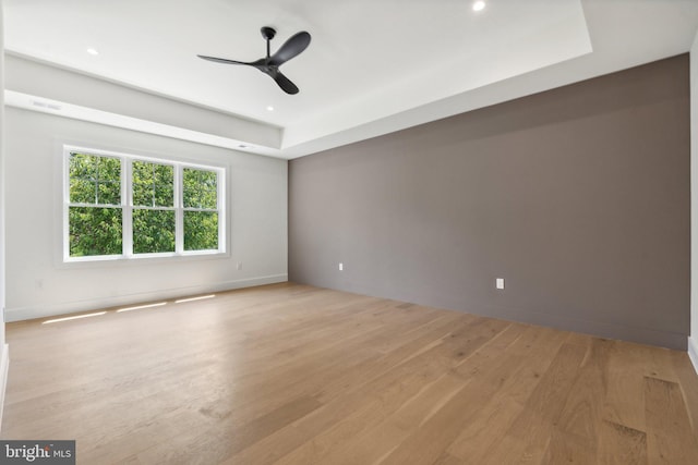 empty room with ceiling fan, light wood-type flooring, and a raised ceiling