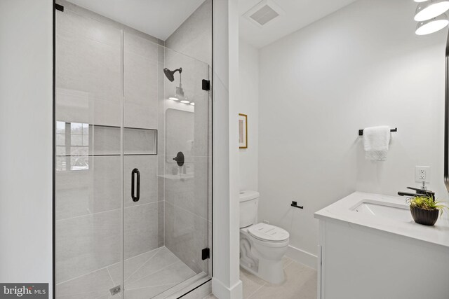 bathroom with a shower with door, vanity, tile patterned floors, and toilet