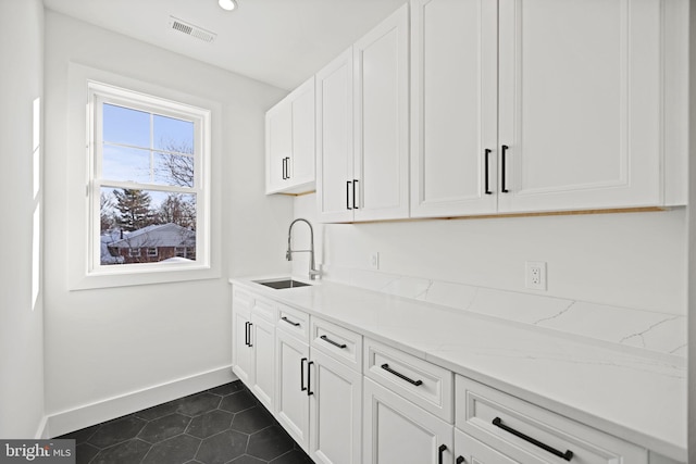 kitchen featuring light stone counters, sink, white cabinets, and dark tile patterned flooring