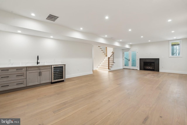 bar featuring beverage cooler, sink, light hardwood / wood-style flooring, and gray cabinetry