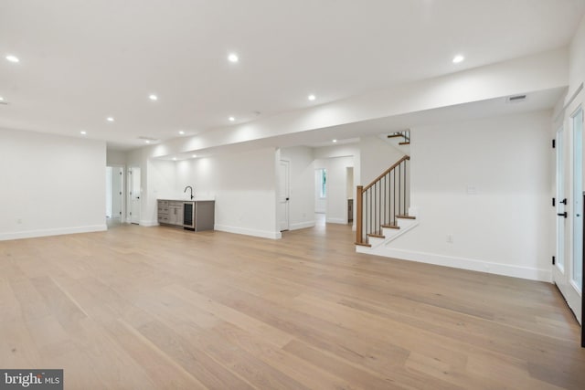 unfurnished living room featuring wet bar and light hardwood / wood-style flooring