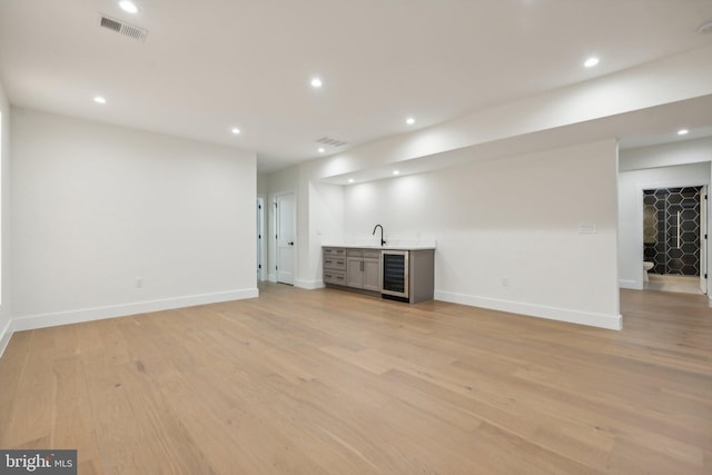 unfurnished living room with wet bar, light hardwood / wood-style floors, and beverage cooler