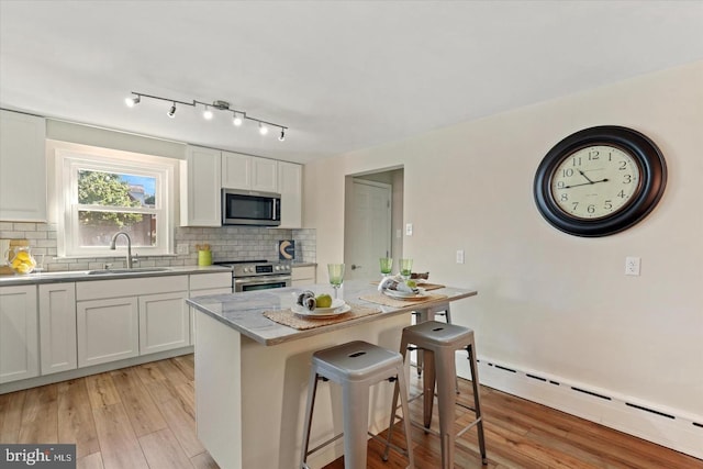 kitchen featuring appliances with stainless steel finishes, sink, white cabinets, light hardwood / wood-style floors, and a baseboard heating unit