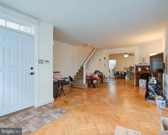 entrance foyer with ceiling fan, a brick fireplace, and light parquet floors