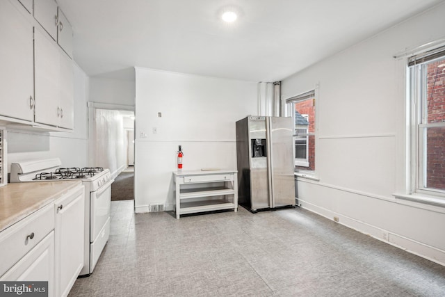 kitchen with white gas range, white cabinets, and stainless steel fridge with ice dispenser